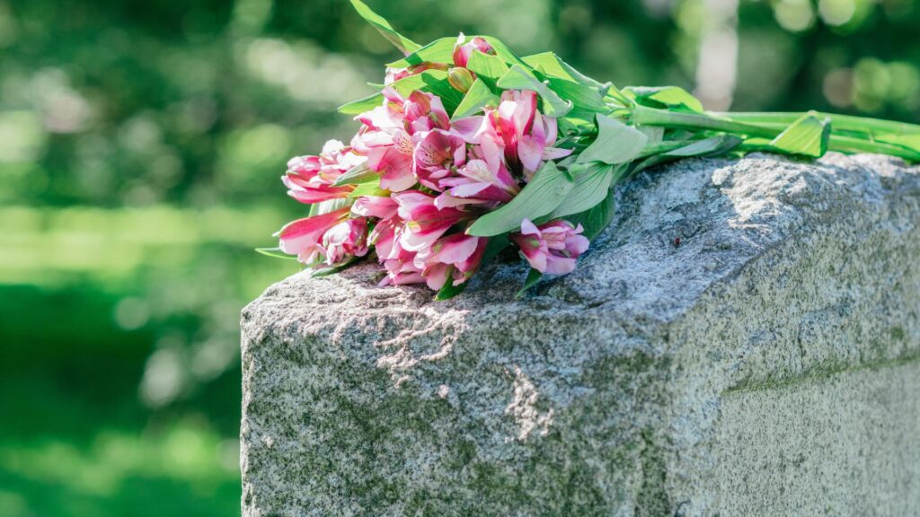 Headstone with pink flowers resting on top of it.