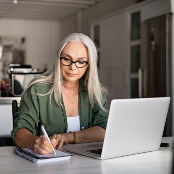 A middle-aged woman taking notes and looking at her laptop